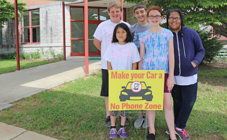 Students with a "Make Your Car a No Phone Zone" sign.